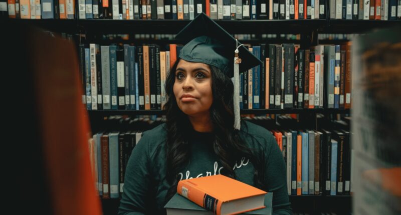 a woman in a cap and gown holding a stack of books