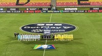 Jugadores de Atlético Bucaramanga y Fortaleza posan en la cancha antes de un partido de la Liga BetPlay, con el logo de la liga en el campo