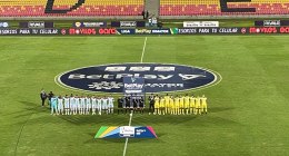 Jugadores de Atlético Bucaramanga y Fortaleza posan en la cancha antes de un partido de la Liga BetPlay, con el logo de la liga en el campo