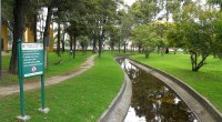 Canal y sendero del Parque Simón Bolívar de Bogotá, con árboles y un letrero del parque