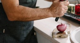 Manos de un cocinero con delantal cortando una cebolla morada en una cocina