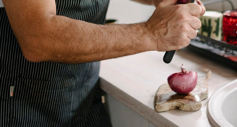 Manos de un cocinero con delantal cortando una cebolla morada en una cocina