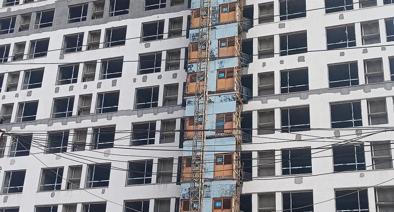 Edificio de vivienda en obra, con ventanas sin terminar y montacargas en la fachada