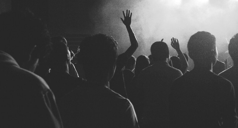 Siluetas de público en un concierto en blanco y negro, con las manos levantadas frente al escenario