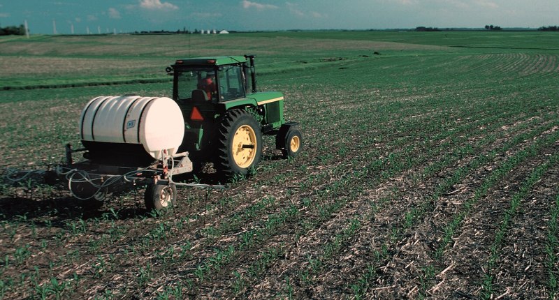 Tractor con tanque de fertilizante recorriendo un campo de maíz recién sembrado