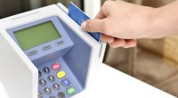 Mano de una persona pasando una tarjeta bancaria azul por un datáfono blanco, en un punto de pago