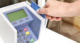 Mano de una persona pasando una tarjeta bancaria azul por un datáfono blanco, en un punto de pago