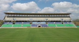 Tribuna del Estadio Jaraguay de Montería, con graderías azules y verdes vacías y la cancha de césped