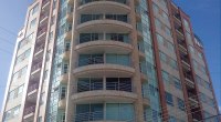 Edificio residencial de apartamentos con balcones curvos y fachada de vidrio, bajo cielo azul