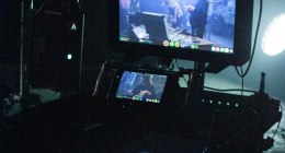 Monitor de cámara en un set de rodaje oscuro, con la imagen de la toma en pantalla y una luz de estudio al fondo