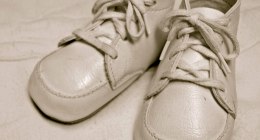 Un par de zapatos blancos de bebé de cuero con cordones, sobre una tela clara, en sepia