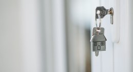 Llaves con un llavero en forma de casa colgando de una cerradura blanca, con el fondo desenfocado