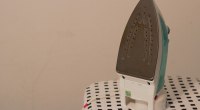 Plancha de vapor sobre una tabla de planchar con estampado de cuadros negros, contra una pared lisa