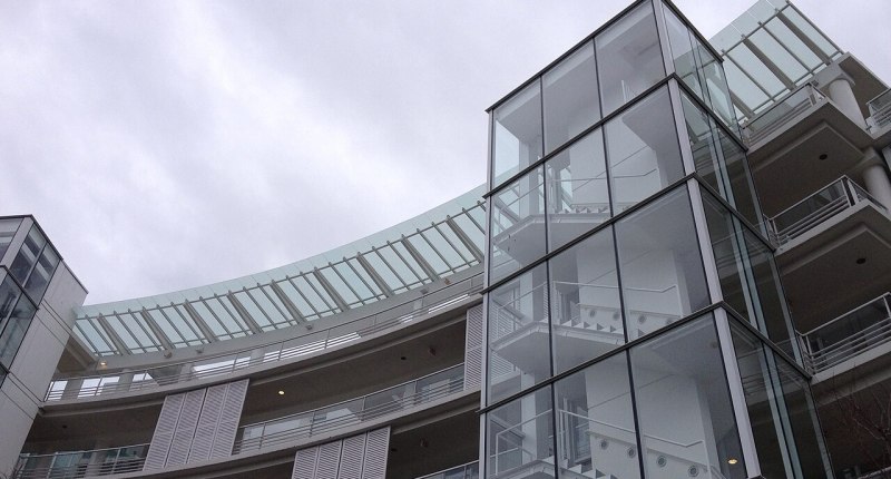 Edificio de apartamentos de fachada curva con balcones y una torre de vidrio, bajo un cielo nublado