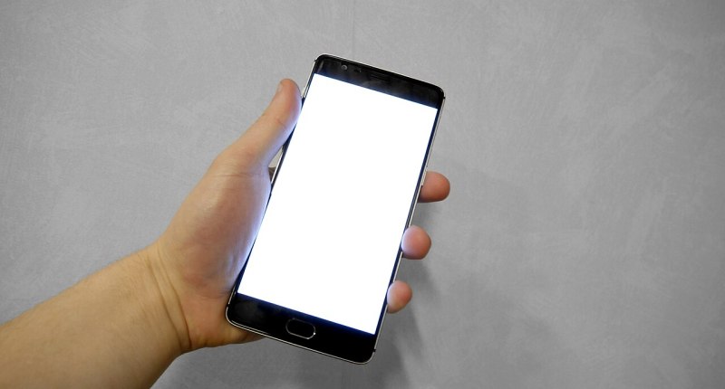 Mano sostiene un celular con la pantalla en blanco frente a una pared gris