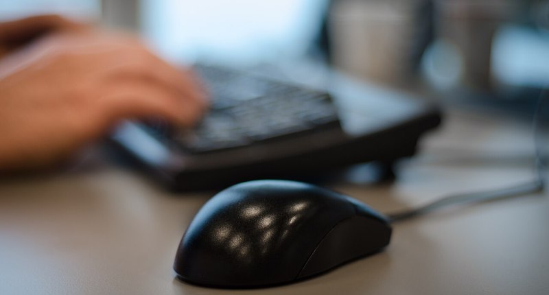 Teclado y ratón de computador de oficina, con una mano borrosa al fondo
