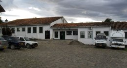 Fachada de un hospital público de Villa de Leyva, Boyacá, con dos ambulancias y otros vehículos estacionados en una plaza empedrada