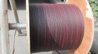 Bobina de cable de fibra óptica negro con franjas rojas, sobre un soporte metálico en la calle