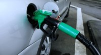 Manguera verde de un surtidor de gasolina cargando un auto plateado en una estación de servicio