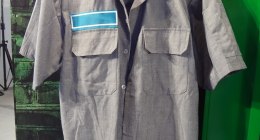 Camisa de trabajo gris de manga corta colgada en un perchero frente a un casillero verde