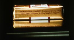 Cajetilla de cigarrillos de lado, sobre fondo oscuro, con la advertencia sanitaria impresa