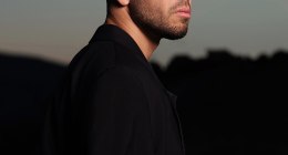 Anyma, productor y DJ, de perfil con camisa negra, con el cielo del atardecer de fondo