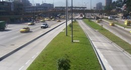 Avenida de Bogotá con varios taxis amarillos, buses y carros en circulación, y un separador con pasto y árboles
