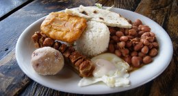 Plato de bandeja paisa con frijoles, arroz, carne, chicharrón, huevo frito, arepa, plátano y chorizo