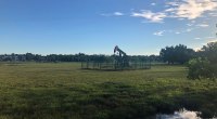 Balancín de un pozo petrolero en un campo abierto con pasto y cielo azul, rodeado por una cerca