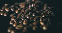 Granos de café tostados, oscuros y brillantes, sobre un fondo negro