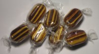 Caramelos rayados de color café y amarillo, envueltos en plástico transparente, sobre una superficie blanca