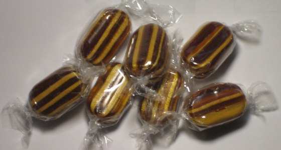 Caramelos rayados de color café y amarillo, envueltos en plástico transparente, sobre una superficie blanca