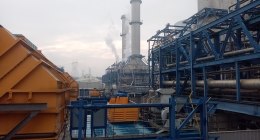 Central térmica de gas con chimeneas y estructuras de acero azul, con humo saliendo de una de ellas