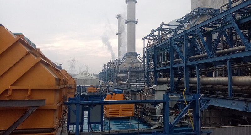 Central térmica de gas con chimeneas y estructuras de acero azul, con humo saliendo de una de ellas