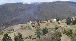 Humo de un incendio forestal sobre una montaña quemada, con un pueblo con iglesia blanca en la ladera (Chíquiza, Boyacá)