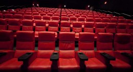 Sala de cine vacía con filas de butacas rojas con brazos negros y una señal de salida al fondo
