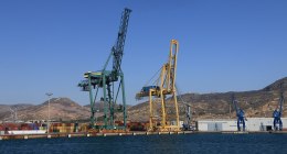 Grúas de puerto y contenedores apilados junto al muelle, con cerros al fondo