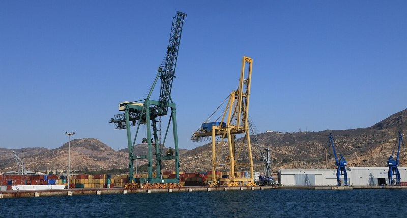 Grúas de puerto y contenedores apilados junto al muelle, con cerros al fondo