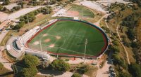Vista aérea de un diamante de béisbol con césped verde y pista roja, en un complejo deportivo