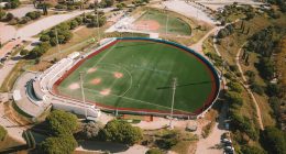 Vista aérea de un diamante de béisbol con césped verde y pista roja, en un complejo deportivo