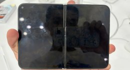 iPhone Duo plegado en la mano de una persona, con la pantalla exterior negra y la bisagra en el centro, en un punto de exhibición
