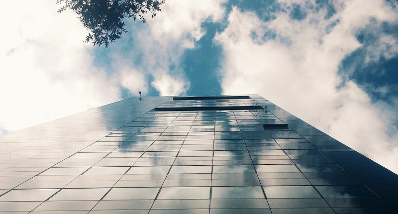 Torre de vidrio de la Bolsa de Valores de Colombia, vista desde abajo, con nubes reflejadas
