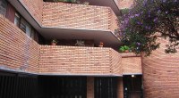 Fachada de ladrillo de un conjunto residencial en Bogotá, con balcones con plantas y un árbol de flores moradas