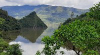 Embalse de La Esmeralda en Chivor, con agua en calma, una montaña que se refleja y vegetación en primer plano