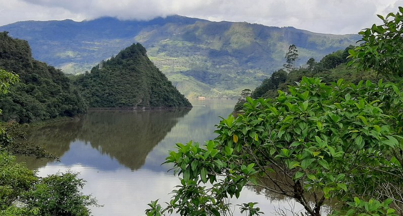 Embalse de La Esmeralda en Chivor, con agua en calma, una montaña que se refleja y vegetación en primer plano