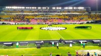 Estadio El Campín de Bogotá de noche, con la cancha iluminada, la graderia amarilla y roja llena de público y telones de la ceremonia en el césped