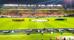 Estadio El Campín de Bogotá de noche, con la cancha iluminada, la graderia amarilla y roja llena de público y telones de la ceremonia en el césped