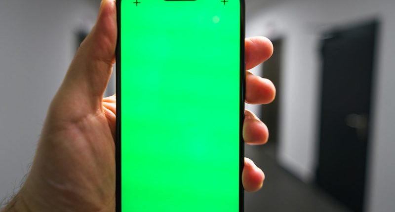 Mano sosteniendo un celular con la pantalla verde en blanco, en un pasillo