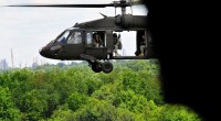 Helicóptero UH-60 Black Hawk del Ejército de EE. UU. en vuelo sobre un bosque, con la puerta abierta y soldados lejanos en el interior