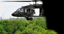 Helicóptero UH-60 Black Hawk del Ejército de EE. UU. en vuelo sobre un bosque, con la puerta abierta y soldados lejanos en el interior